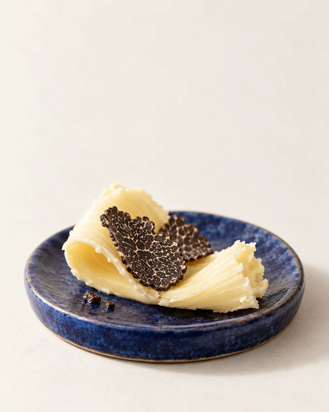 Copeaux de beurre et lamelles de truffe noire sur une assiette bleu cobalt