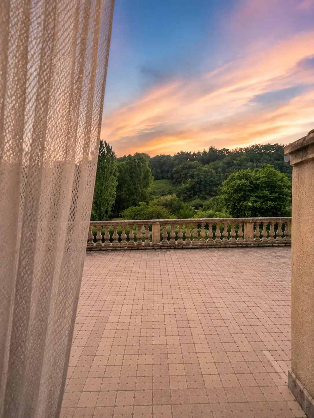 Terrasse de Côté Source avec balustrade en pierre et vue sur les collines au coucher du soleil