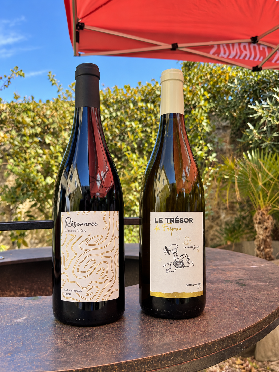 Bouteilles Résonance et Le Trésor de Fripon sur une table sous un parasol rouge